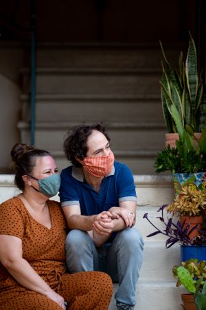 Portrait of man and woman sitting on apartment stairs holding hands and looking out