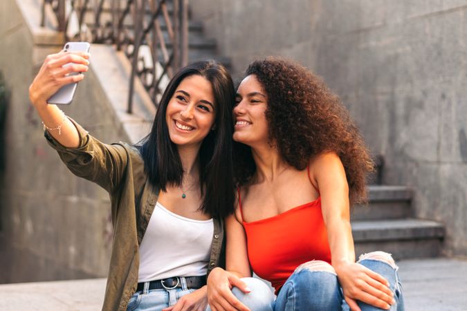 two happy women sitting on a stairs taking a selfie