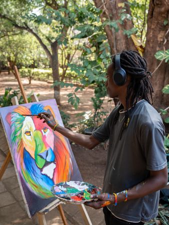 Black male painter painting a colorful lion standing on a park