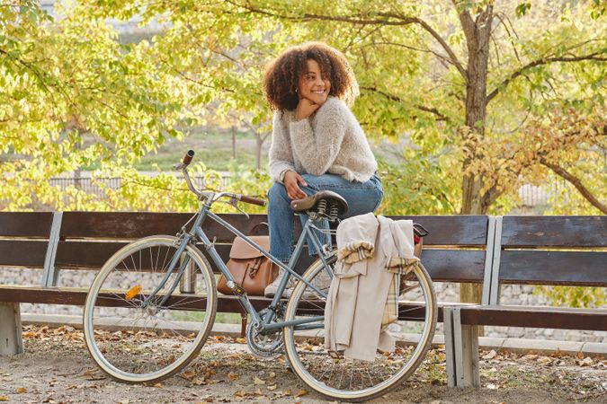 Smiling Black Latina woman sitting on bench near bicycle in park