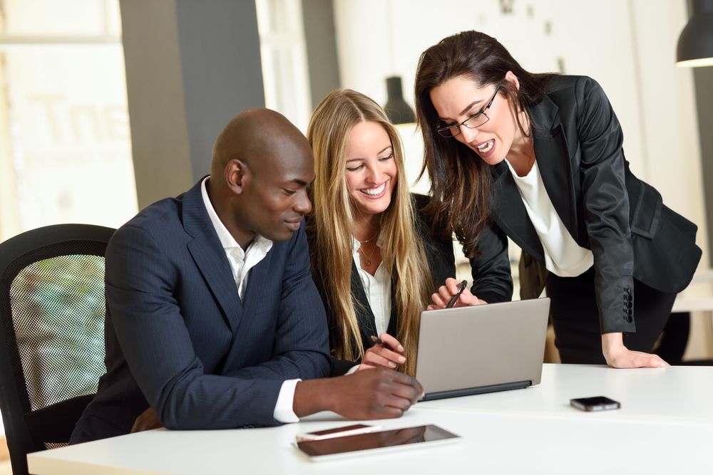 Three colleagues working together in office around a laptop