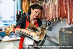 Woman in butcher shop slicing meat 0KqaD4