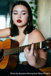Close up of young woman’s hands playing chord on acoustic guitar 48BLK0