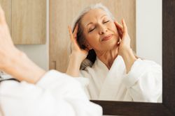 Female in bathrobe doing face massage in bathroom
