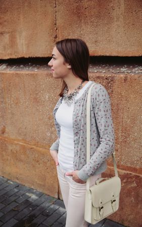 Woman wearing gray jacket, pink jeans and satchel bag over a stone wall background