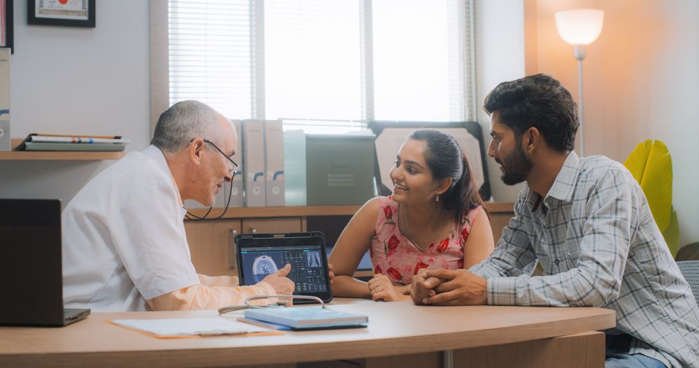 Indian Couple in a Doctor Visit in a Private Clinic: Professional Physician Using Digital Tablet to Explain MRI Results to Patients