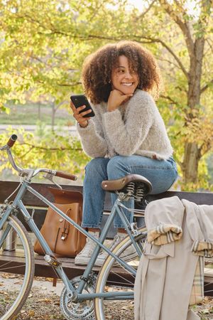 Smiling Black woman using smartphone on bench in park