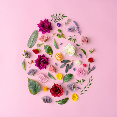 Easter egg shape made with various spring flowers and leaves on pastel pink background