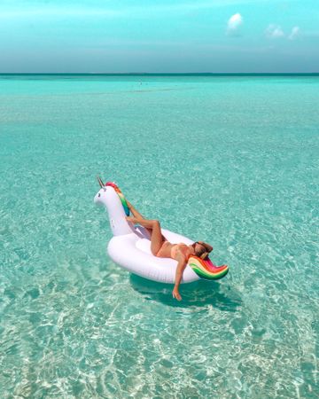Woman in bathing suit lying on an inflatable unicorn floating on sea surface  during daytime