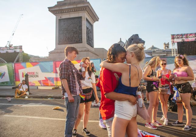 Two young lesbian women hugging in street during London Pride in Trafalgar Square