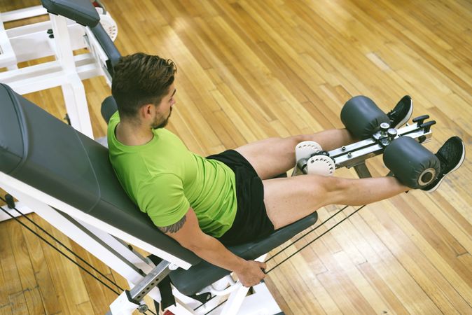 Looking down at muscular male in green t-shirt working out using leg extension machine