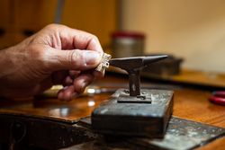 Goldsmith creating and repairing in his crafting gold jewelry workshop with an anvil. Jeweler working in a silver jewel.