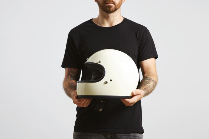 Man in plain dark t-shirt and dark jeans holding motorcycle helmet