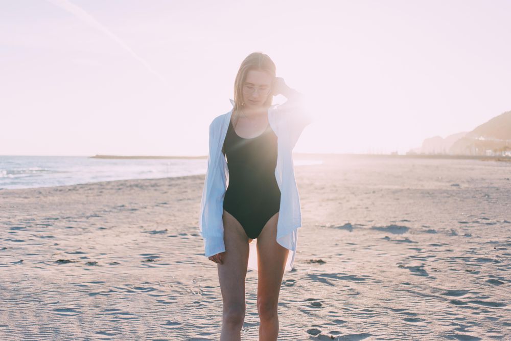 Young woman standing on beach with sunset at her back