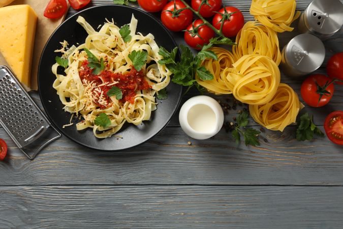 Composition with plate of tasty pasta and ingredients for cooking on wooden background