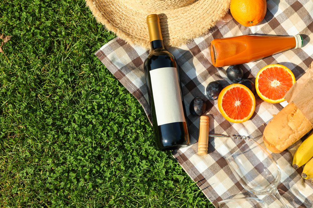 Bottle of wine, baguette, fruits, straw hat and towel on grass, space for text