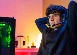 Young male gamer with headphones leans back in chair with arms behind head with satisfied face.