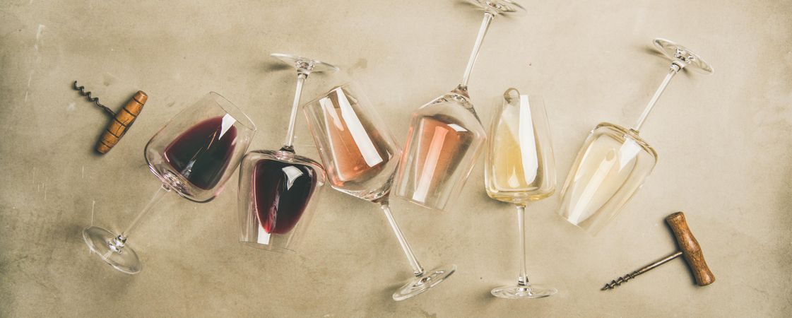 Glasses of wine on grey background with corkscrews, wide composition