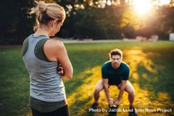 Female trainer standing in the park with man doing weight training with kettlebell 4dP2E4