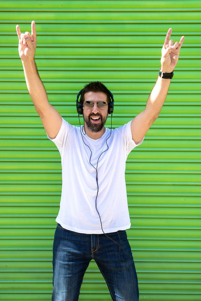 Man in headphones and glasses pointing up in front of green background