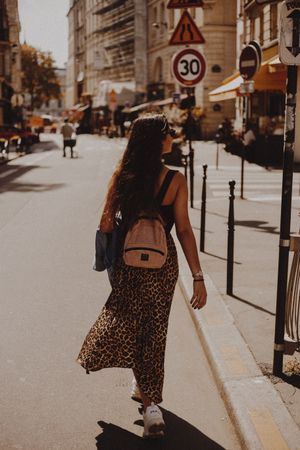 Back view of woman in long skirt with backpack walking on street during daytime
