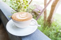 Closeup of cup with hot latte art on top wooden board in garden with lighting on top right side