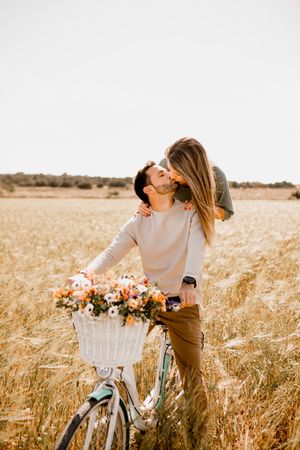 Playful lovers riding bicycle on wheat field