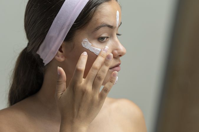 Close up profile of a young woman applying moisturizing cream during her beauty routine
