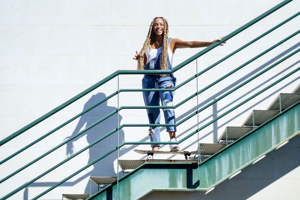Smiling female in denim overalls standing on skateboard on stairs