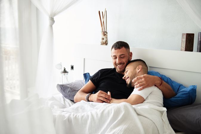 Smiling gay couple hugging on bed