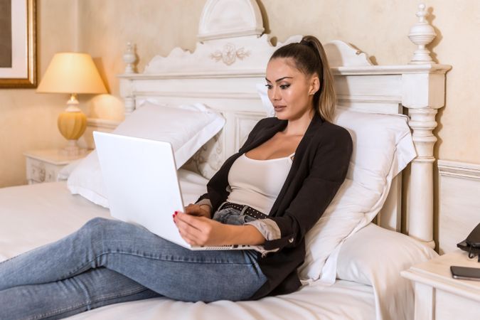 Woman using computer sitting in bed in a hotel room