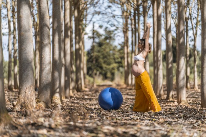 Adult pregnant woman training with pilates ball in park during sunny day