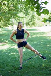 A woman is working out outside using a resistance band in a sunny park, surrounded by greenery and trees