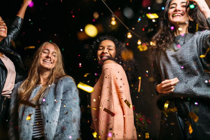 Happy multi-ethnic women throwing confetti at a party outside