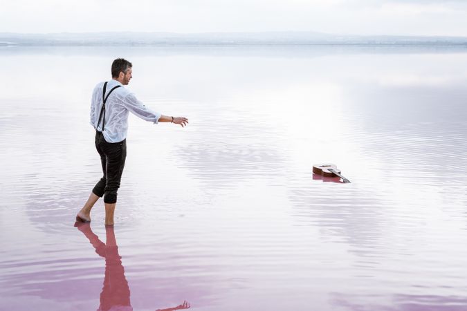 Modern man in wet shirt picking up guitar floating in water