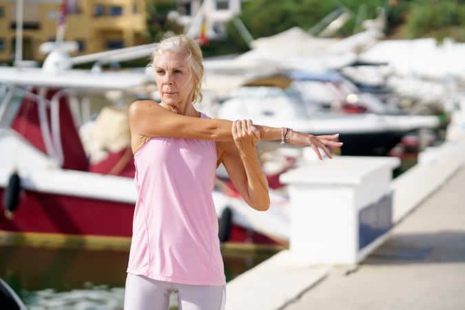 Older female in pink athletic wear stretching her arms after workout