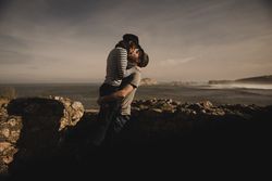 Man kissing and holding woman on hands near stones on shore
