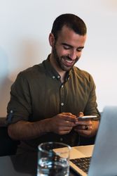 Happy man browsing smartphone near laptop