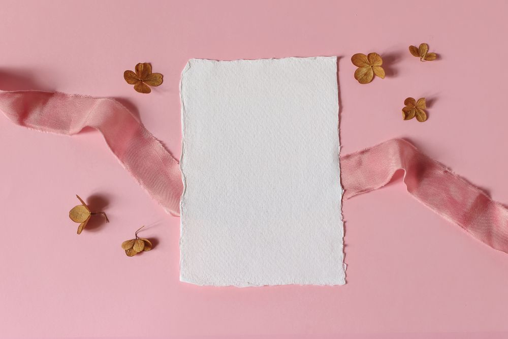Cotton greeting card, dry hydrangea flowers and satin ribbon on pink table background