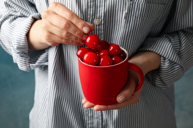 Woman holds cup with fresh red cherry, close up