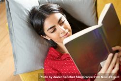 Woman lying on pillows reading a green book 49z26b