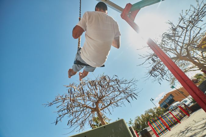Man swinging on playground in sunlight