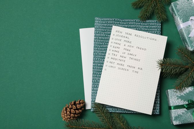 Gift boxes, paper with list and decorations on green background, space for text