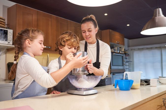 Mother with kids sifting flour for dough in bowl