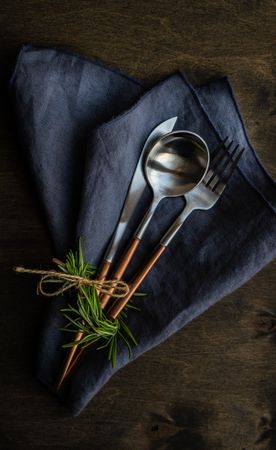 Cutlery set on navy napkin with rosemary garnish