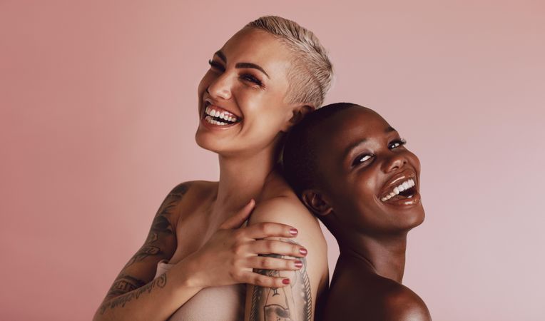 Two women with buzz cut hairstyle standing back to back and smiling at camera