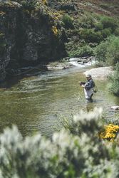 Confident man fishing with rod while standing in river stream