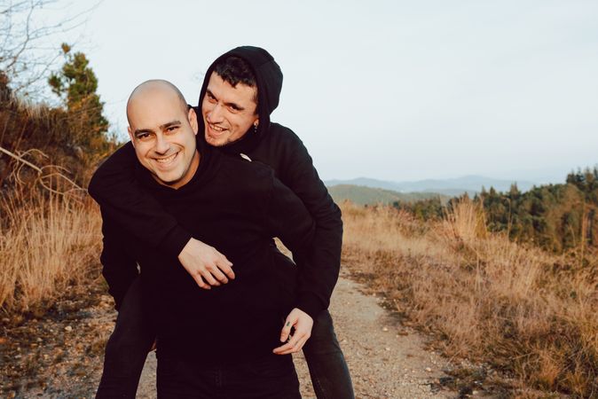 Smiling man holding on back cheerful guy on road on hill