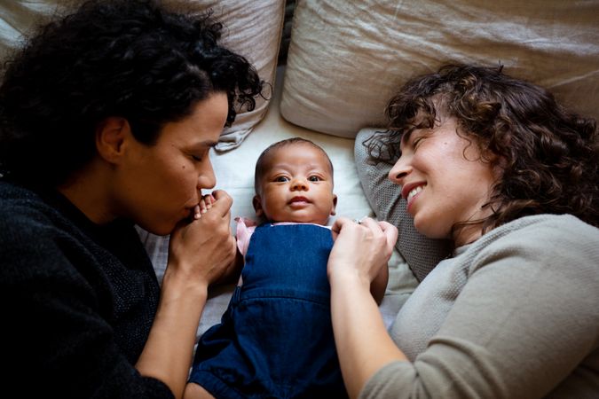 Two woman lying with cute baby kissing baby’s hand