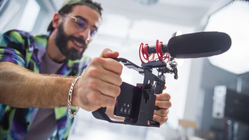 Focused Young Male Filmmaker With Beard, Adjusting Camera Equipment In Studio, Capturing Content For Advertising Project, Showcasing Diversity And Creativity In Modern Cinematography.